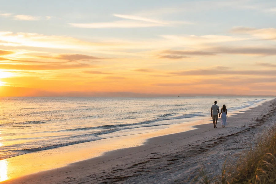 Couple walks along sandy beach at sunrise beside ocean waves