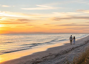 Couple walks along sandy beach at sunrise beside ocean waves
